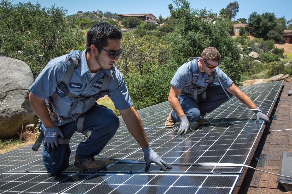 Two Mauzy technicians installing solar panels on the roof of a residential home
